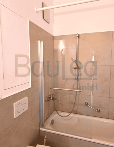 Badsanierung München NACHHER – Badewanne mit Glasduschbtrennung, graue Wandfliesen, WC